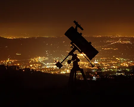 A telescope in silhouette above a city at night