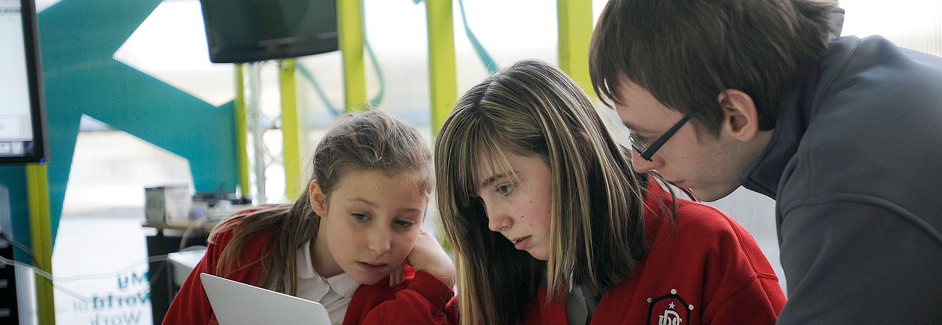 Two girls look use a laptop for coding with the help of a GSC instructor