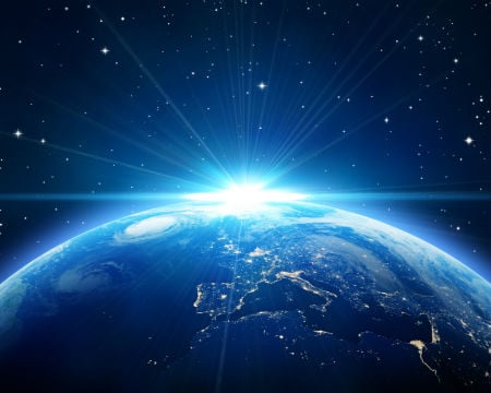 The sun rises above Earth as viewed from a distance in space