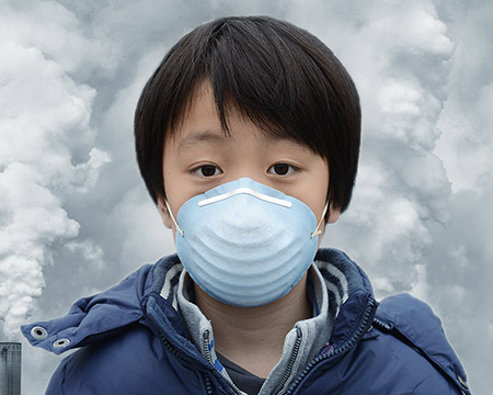 A child wearing a mask stands against a backdrop of plumes of gas rising into the sky from tall chimneys