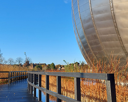 A wooden boardwalk curls through the wetlands surrounding the IMAX building at Glasgow Science Centre