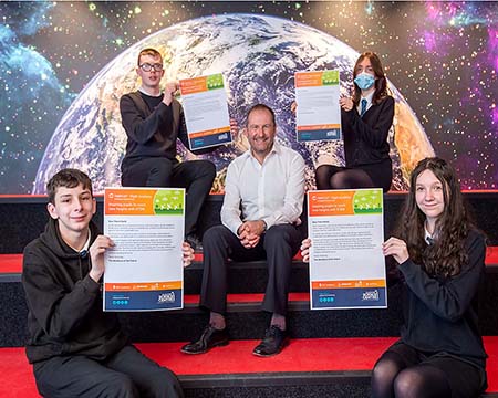 Four seated students each hold a promise against the backdrop of an Earthrise. Seated in the centre of the photo is Dr Stephen Breslin.
