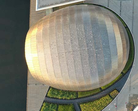 IMAX Theatre at Glasgow Science Centre - aerial view shows top of titanium shell and sun rays reflecting out onto still waters of Canting Basin.