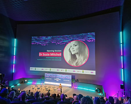 A speaker at the on-stage podium in front of the huge screen and a seated audience in the IMAX. Image: CAN DO Fest 2023