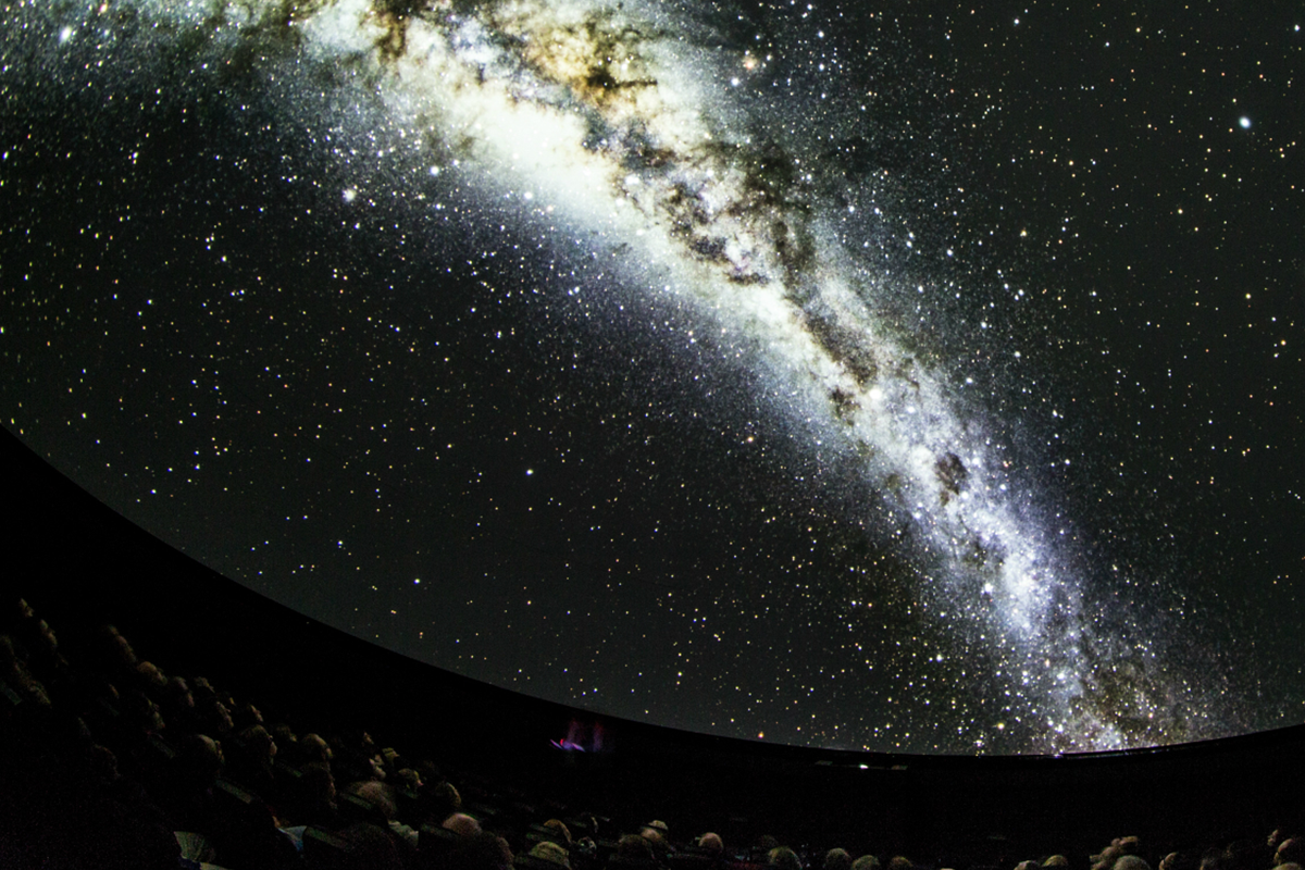 A planetarium audience look up at images of space