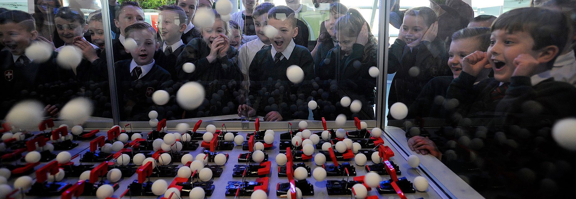 School pupils watch on in excitement as ping pong balls fly everywhere in a chain reaction demonstration