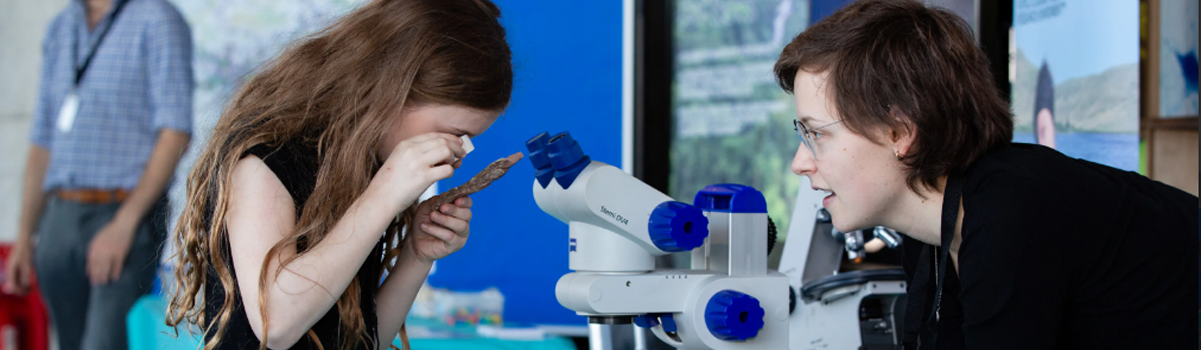 Child looks through microscope whilst expert explains what they're looking at