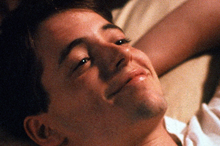 A young man lies smiling with hands behind his head.