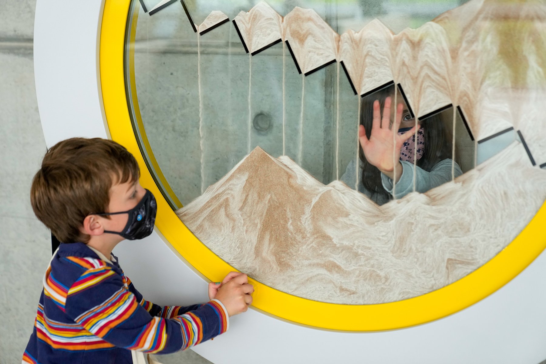 Two young people watch on as different coloured sand forms patterns as it flows through an obstacle