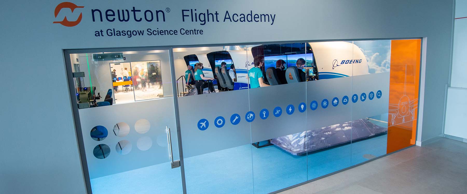 Looking through a window into the Newton Flight Academy where there are three full motion flight simulators with school pupils at the controls.