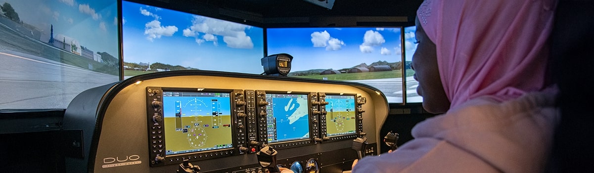 A person at the controls of the flight simulator looking at the four screens that make up the windscreen