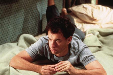A man lies daydreaming on a bed with arms crossed.