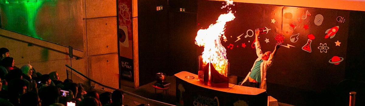Visitor Experience Assistant enthusiastically waving their arms as fire rises from an experiment during a science show