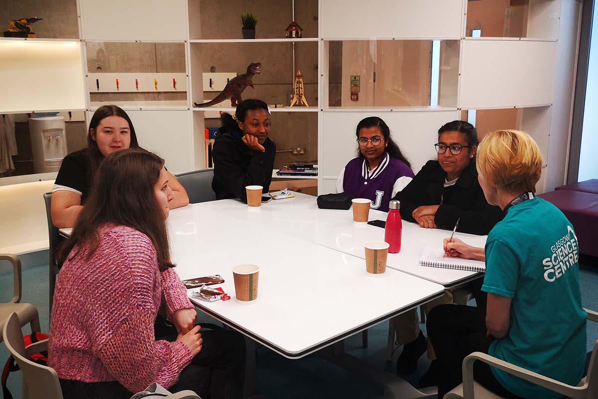 A group of young people and science centre staff member sit around a table in The Bothy.