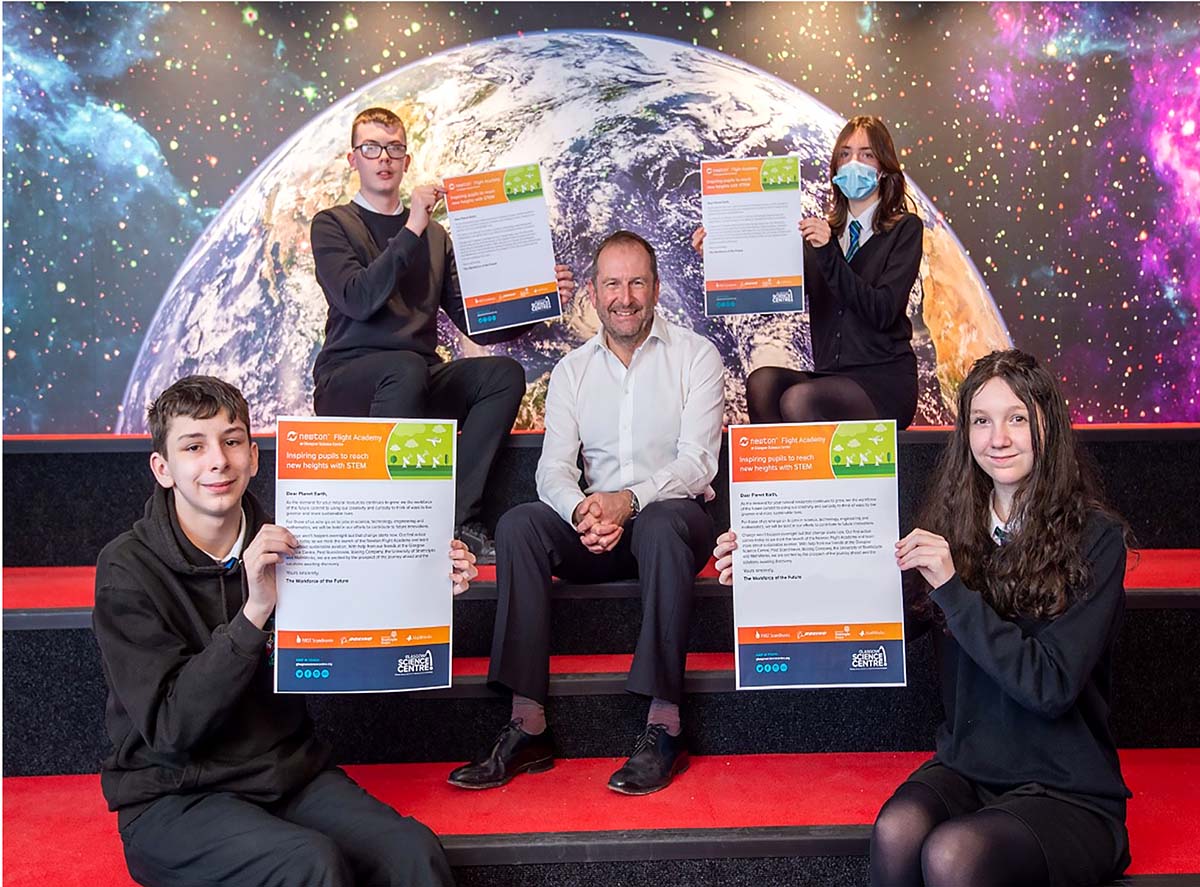 Four seated students each hold a promise against the backdrop of an Earthrise. Seated in the centre of the photo is Dr Stephen Breslin.