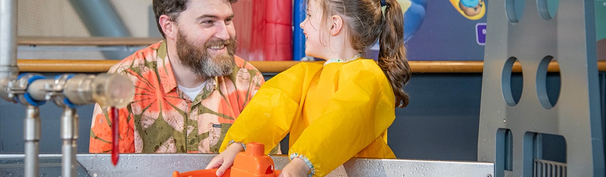 A family smile as they play at a water table. Photo: Paul Watt