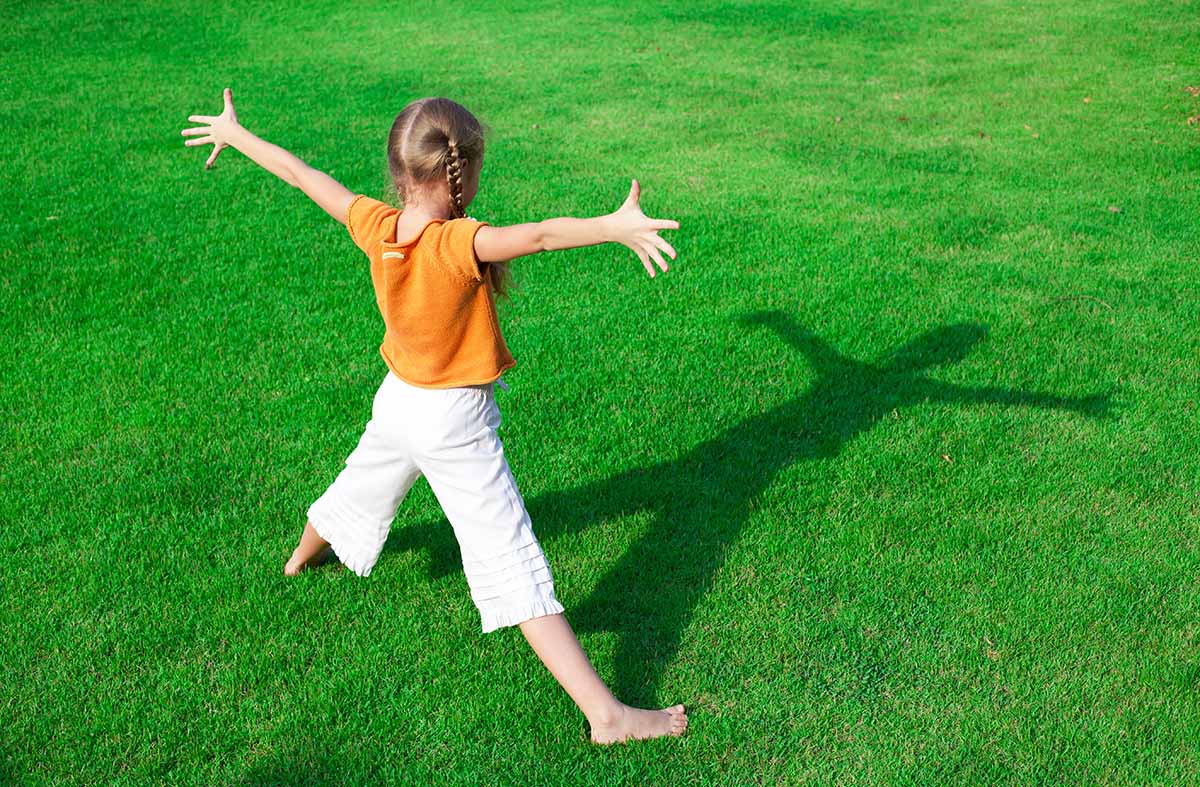 A young person with outstretched arms casts a shadow across a field