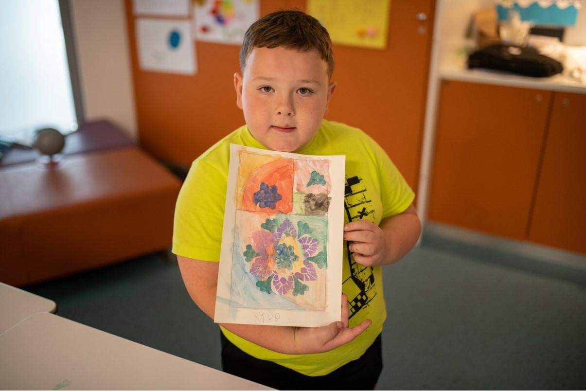 A young person holds a picture they've made using maths