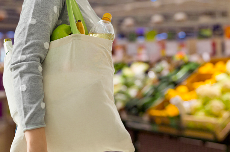 Person carries canvas bag filled with groceries through supermarket