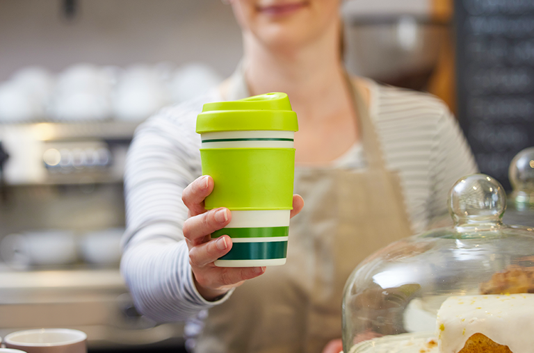 Barista holds out refillable coffee cup towards camera