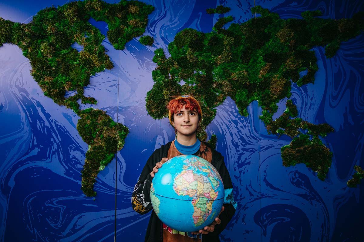 A young person standing against the backdrop of a Earth holds a globe