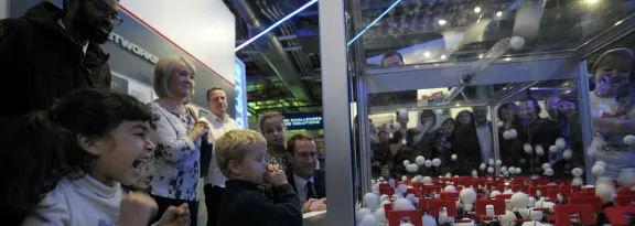 A crowd of mixed ages watch on in excitement at an exhibit demonstrating a chain reaction 