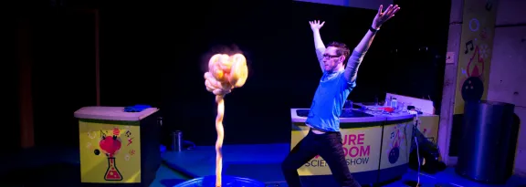 A science communicator on stage performing the Elephant's Tootpaste demo. A plume of 'toothpaste' rises up to almost the same height as the presenter.