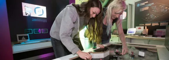 Two women guide the path of light using mirrors at an exhibit in QuantIC