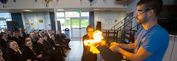 A science communicator and pupil produce a flame in an experiment in front of an audience