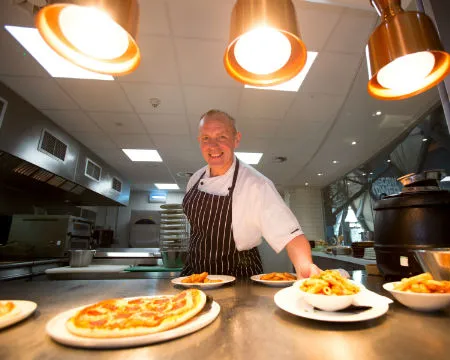 A chef presents plates of food under hot lamps