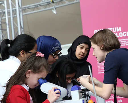 A group of school children looking through microscopes and talking to a STEM professional.
