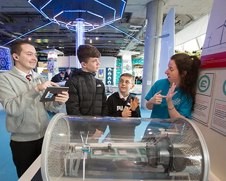 A group of visitors and a science communicator using BSL at an exhibit demonstrating energy from the wind.