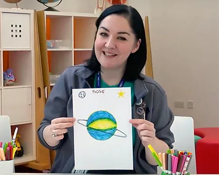 Veronica holds up a picture of a planet she has drawn.
