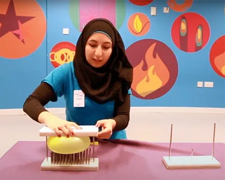 Presenter, Zayneb, sandwiches a ballon between some wood and nails.