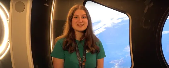 Presenter Natalie sits in front of the Cupola exhibit at Glasgow Science Centre with a view of Scotland/