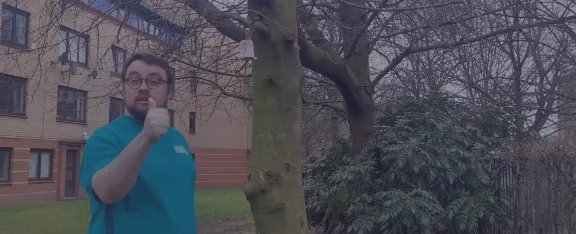 Presenter Sam beside a bird feeder on a tree