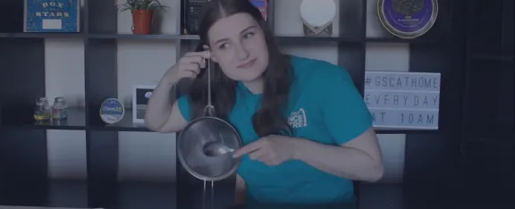 Presenter Natalie holds a piece of string, attached to a kitchen utensil, to her ear