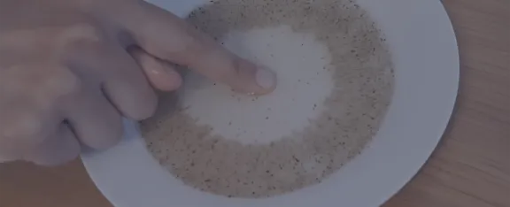 Pepper particles spread out across a bowl of water as a finger coated in soap approaches