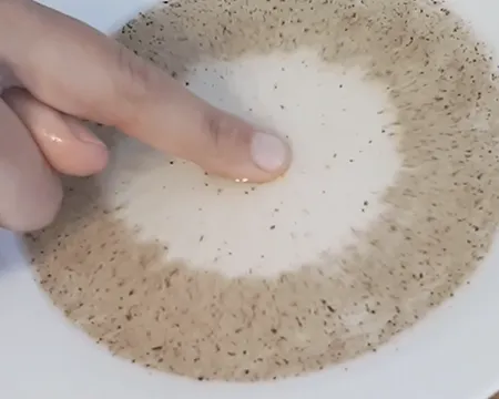 Pepper particles spread out across a bowl of water as a finger coated in soap approaches