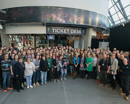 A photograph shows a large number of staff at Glasgow Science Centre in a semi-circle.