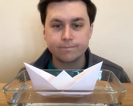 Ross looks at a paper boat floating on water.