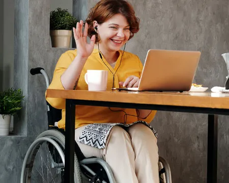 Woman in Orange Tank Top Sitting on Black Wheelchair using Laptop