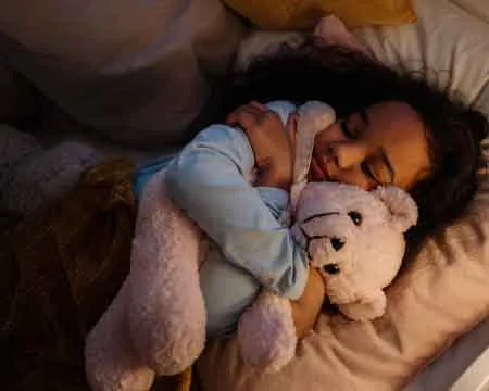 Girl in Blue Long Sleeve Shirt Lying on Bed With White Bear Plush Toy