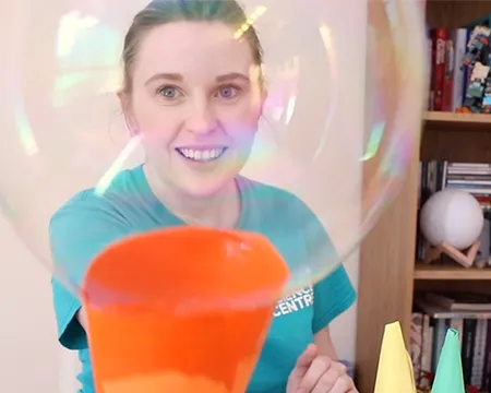 A bubble emerges from an orange-coloured paper bubble blower