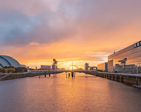 A photo of the sunrise looking east along the River Clyde from a bridge. The sky is yellow, blue and purple and reflected on the surface of the water. Image: Paul Upward and Timberplay Scotland.