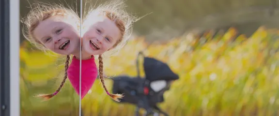 A young child's smiling face appears reflected in a mirror outside. Image: Paul Upward and Timberplay Scotland.