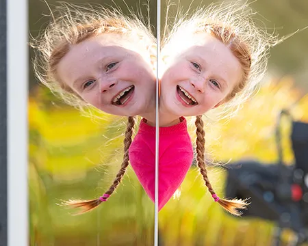 A young child's smiling face appears reflected in a mirror outside. Image: Paul Upward and Timberplay Scotland.