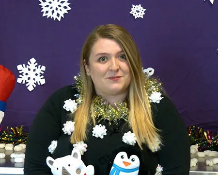 A science communicator in a Christmas jumper surrounded by paper snowflakes