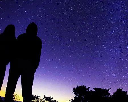 The silhouettes of two people looking up into a starry night sky