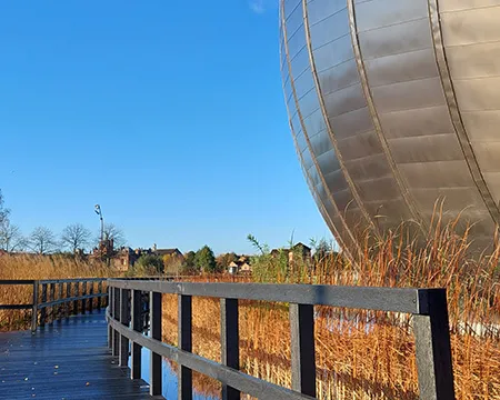 A wooden boardwalk curls through the wetlands surrounding the IMAX building at Glasgow Science Centre